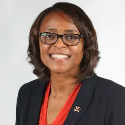 Headshot of a smiling woman with glasses wearing a dark blazer over a red top, featuring a University of Virginia lapel pin.
