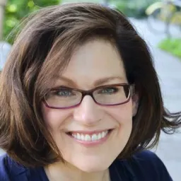 A smiling woman with shoulder-length brown hair wearing glasses.