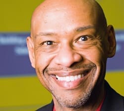 A middle-aged man with a shaved head smiles broadly at the camera.